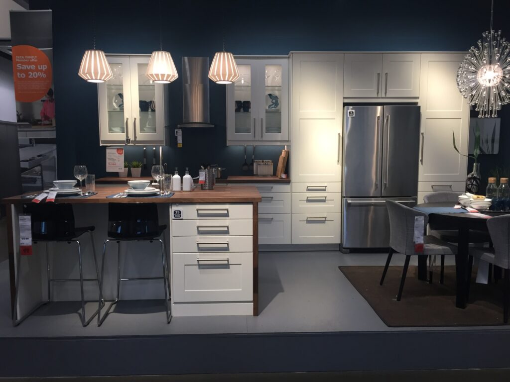 IKEA New Haven Kitchen display, white cabinets with a wood grain top and waterfall edge. Lighting options used are pendant lights and under cabinet and in cabinet lights 